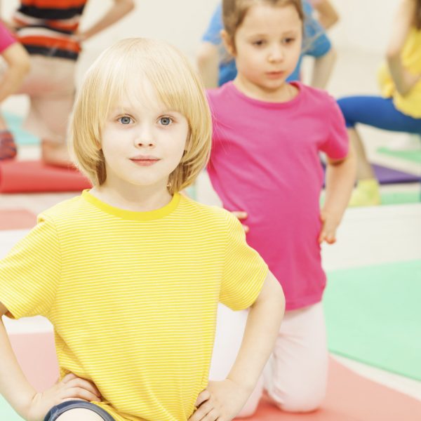 Portrait of Caucasian kid boy kneeling with hands on waist, practicing gymnastics in kindergarten